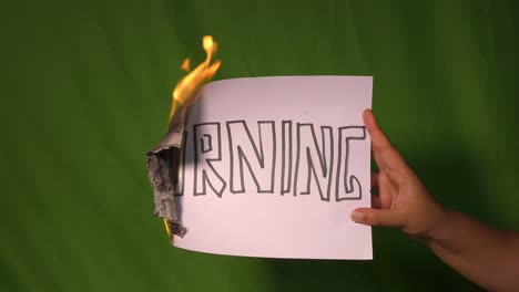 a hand holds the burning paper with burning text word on it