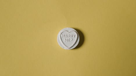 hand picking up heart candy with marry me message on yellow background