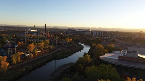 Toma-Aérea-De-Drones-Que-Revela-El-Parque-Acuático-Temático-Elitch-Garden-Con-Vista-De-Edificios-Importantes-En-El-Fondo-Durante-La-Puesta-De-Sol,-Denver,-Colorado