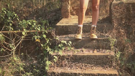 legs of a young brunette woman in yellow boots on some concrete steps in a rural area