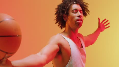 video of biracial male basketball player holding ball cheering on orange to yellow background