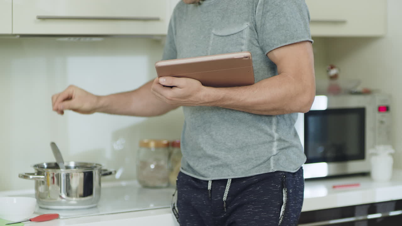 las manos de un hombre en primer plano con una tableta cocinando comida saludable en la cocina del hogar.