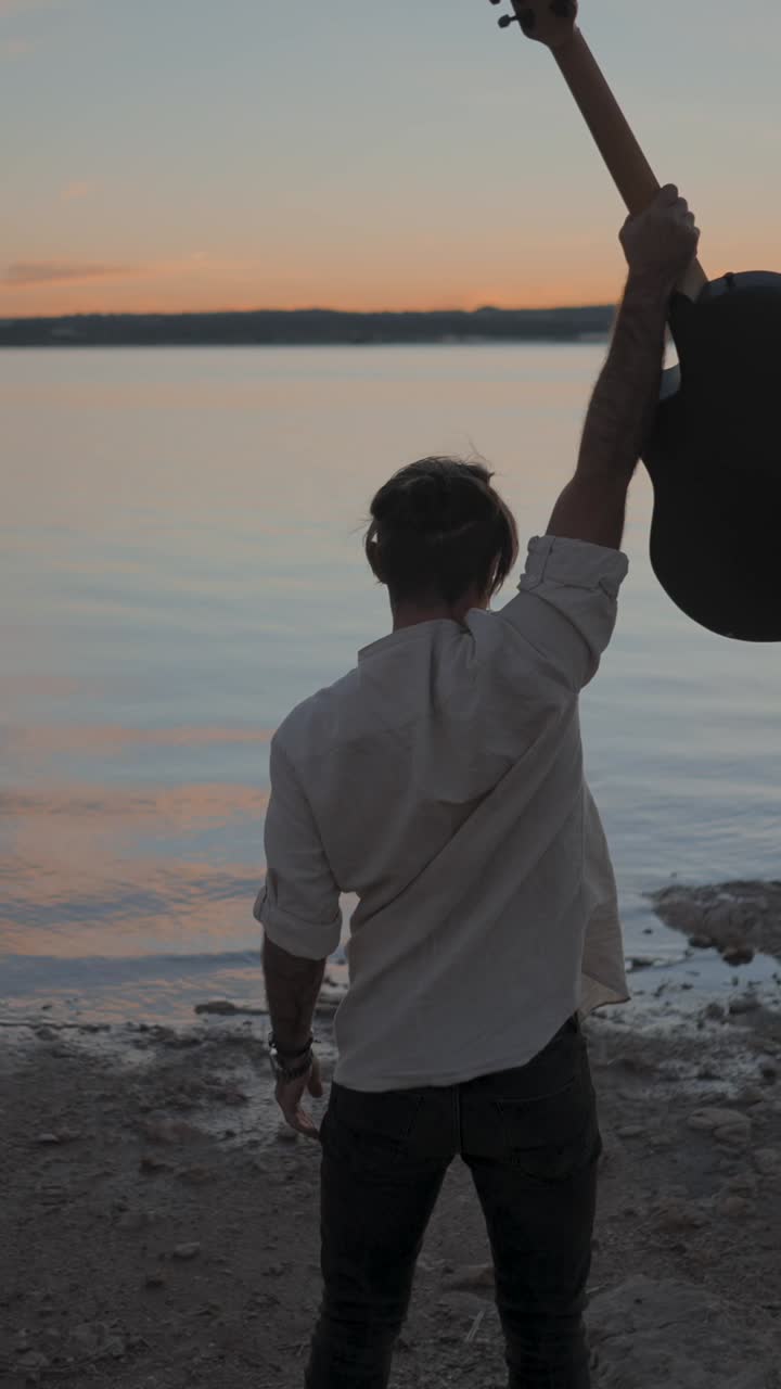 Man holding a guitar at sunset by the water