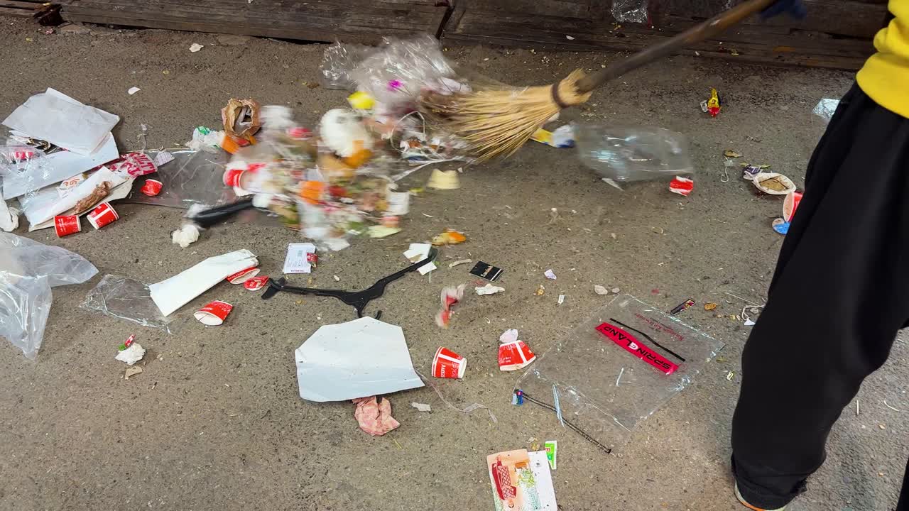 Attività di igiene urbana con un lavoratore che spazza rifiuti di plastica e spazzatura dalla strada.