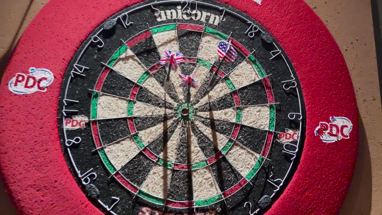 Darts fly toward dartboard in warmly lit bar, camera moves closer for dramatic close-up