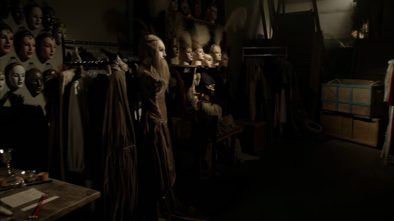 Dunkle Backstage-Garderobe voller Kostüme, Kostümkuratorin inspiziert Schaufensterpuppen und Masken, historische Kleider.