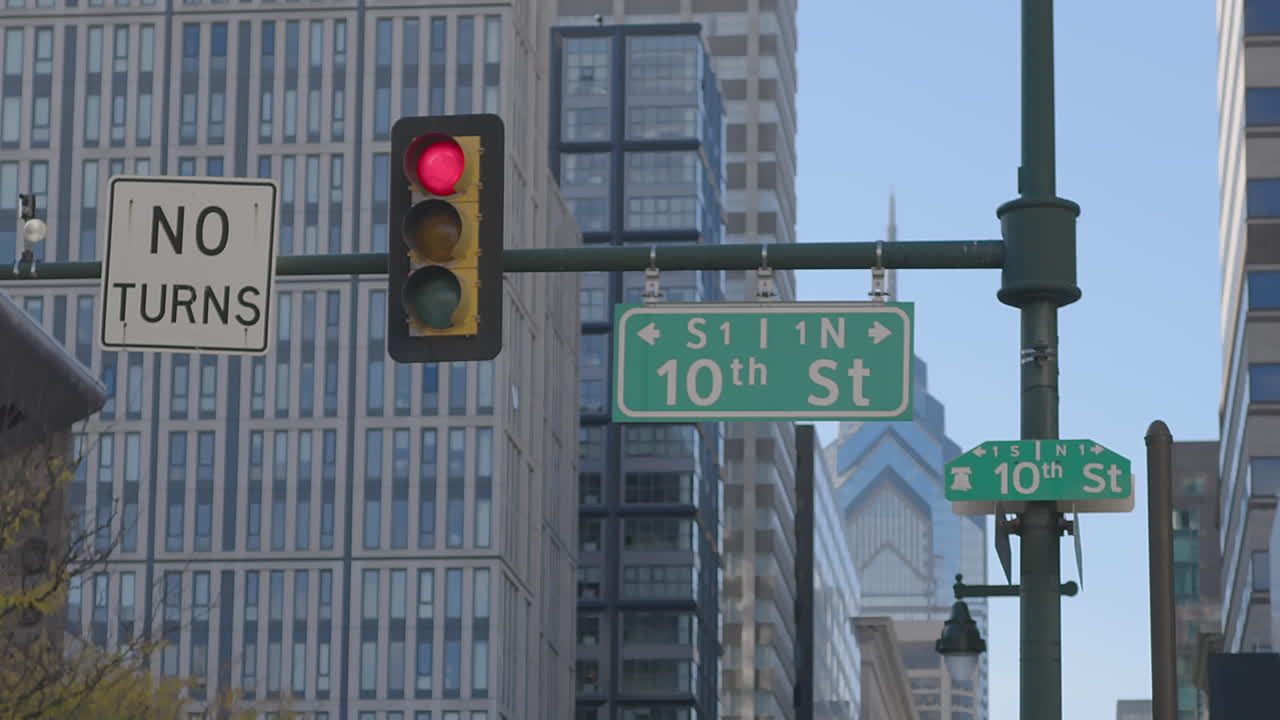 Slow-motion shot of the 10th Street sign and red light in Philadelphia, framed by towering buildings and a crisp sky, capturing the city's structured calm and urban geometry in a quiet moment.