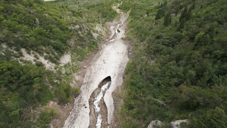 Aerial-view-looking-down-over-craggy-glacial-riverbed-with-rock-opening-to-ice-caves-in-Provo,-Utah