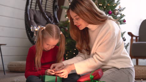 madre e hija envolviendo regalos de navidad sentadas en el suelo cerca de un árbol de navidad en la sala de estar