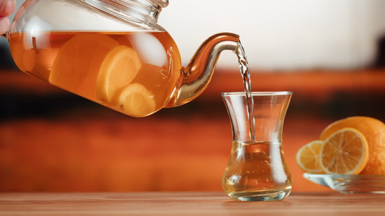Pouring hot lemon tea from a glass teapot into a glass cup