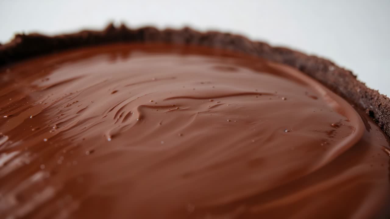 Recording round chocolate tart showing ganache rippling and settling on light tabletop, crumb rim