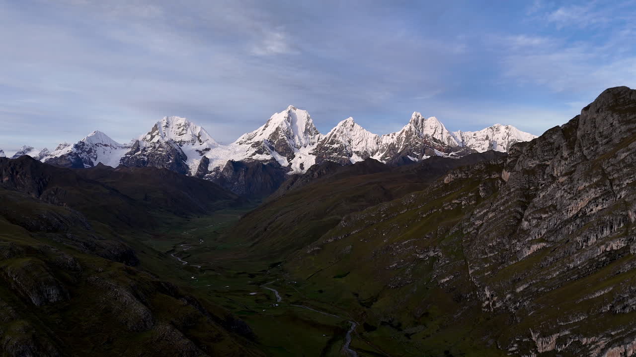 Cinematic aerial view of snowy Andes mountains in Peru with glaciers, rocky cliffs, and hidden blue alpine lake under misty clouds, dramatic landscape and natural travel destination