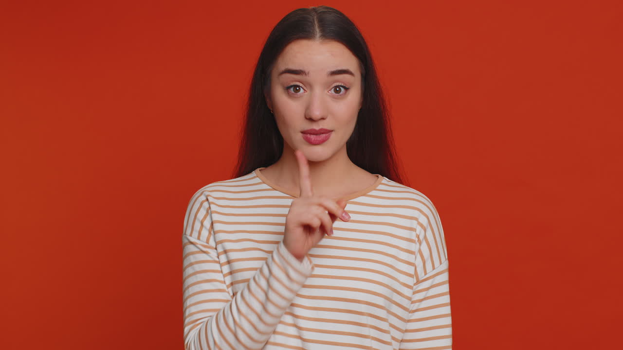젊은 여성은 집게손가락을 입술에 대고 침묵을 지킨다. 비밀을 말하지 말고 조용히 해라