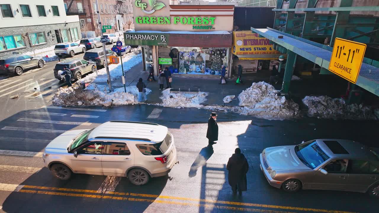 New York, USA, 9 febbraio 2026: Vista sopraelevata di un incrocio cittadino soleggiato con neve che si scioglie. Una prospettiva dall'alto di auto e una persona in abiti tradizionali che attraversano una strada cittadina bagnata.