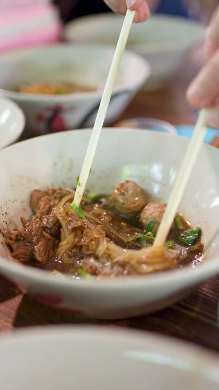 Primer plano de manos usando palillos para comer sopa tradicional tailandesa de fideos con carne en el interior.