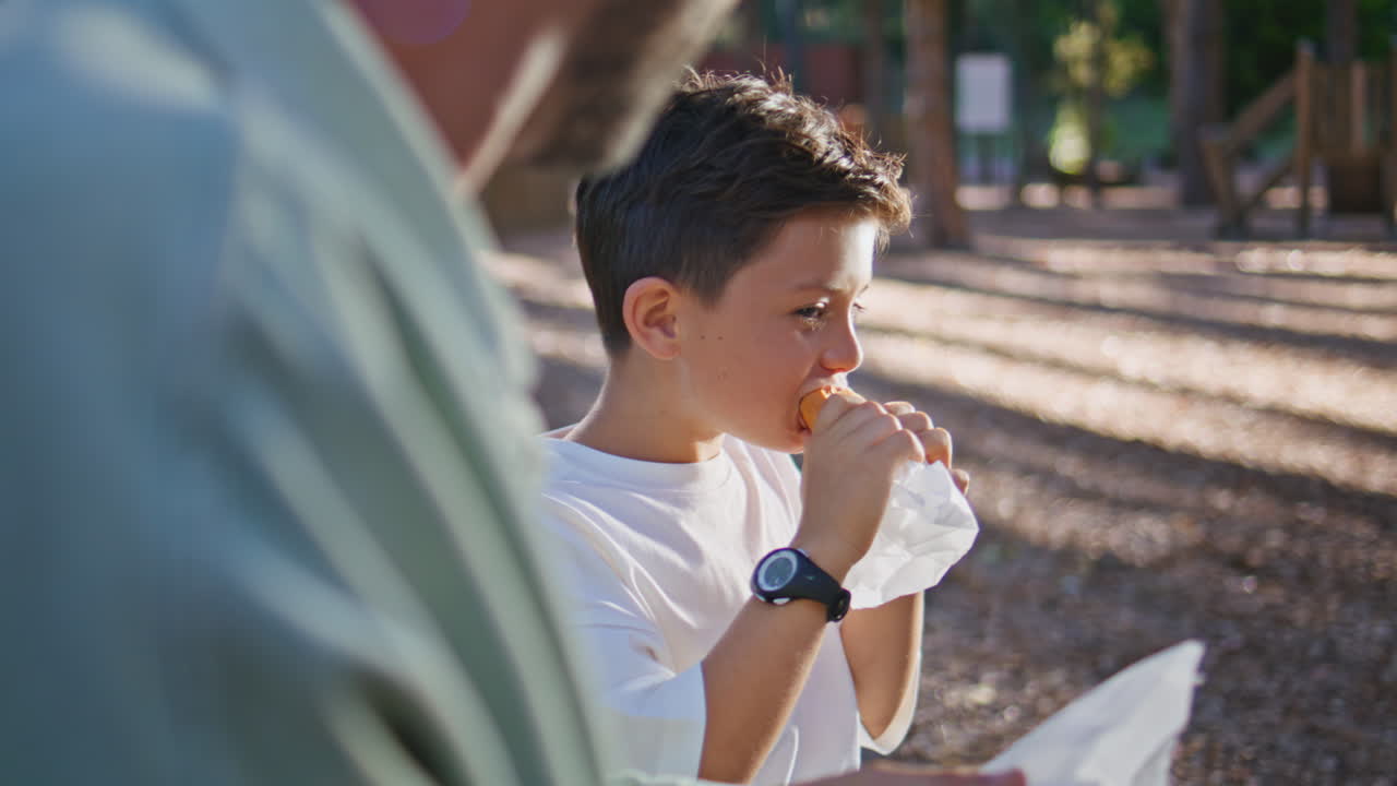 Cute child eating sandwich with loving father at sunny forest picnic closeup