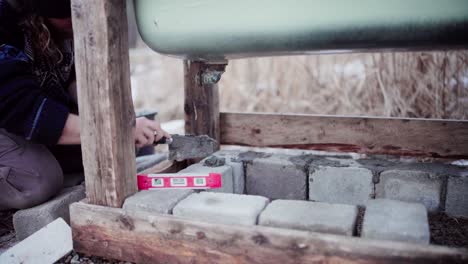 the man is using cement to fill the gaps between the concrete blocks beneath the diy hot tub - close up