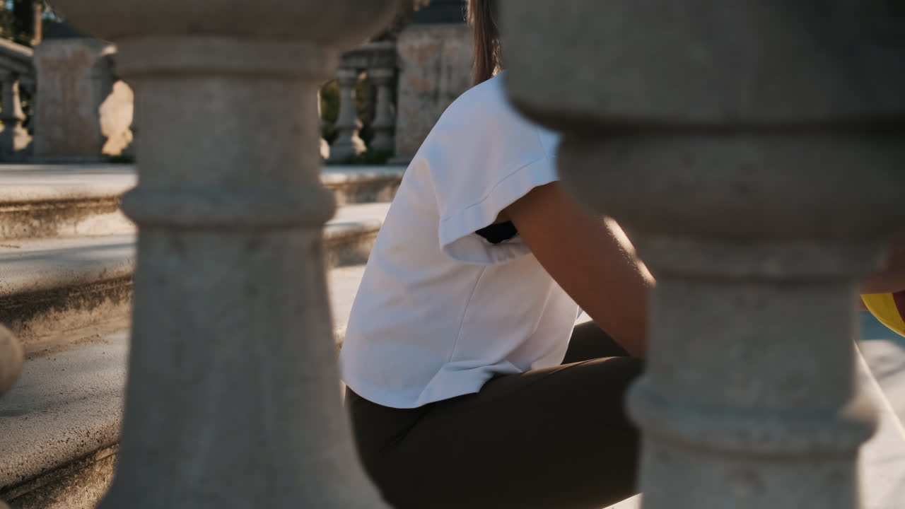 hermosa mujer con la pelota en las manos sentada en las escaleras en el parque de la ciudad.
