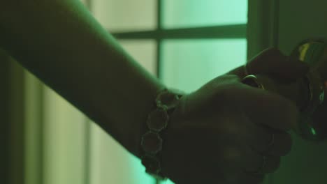 a woman's hand shakily reaches to turn a door knob. something is glowing behind the door.