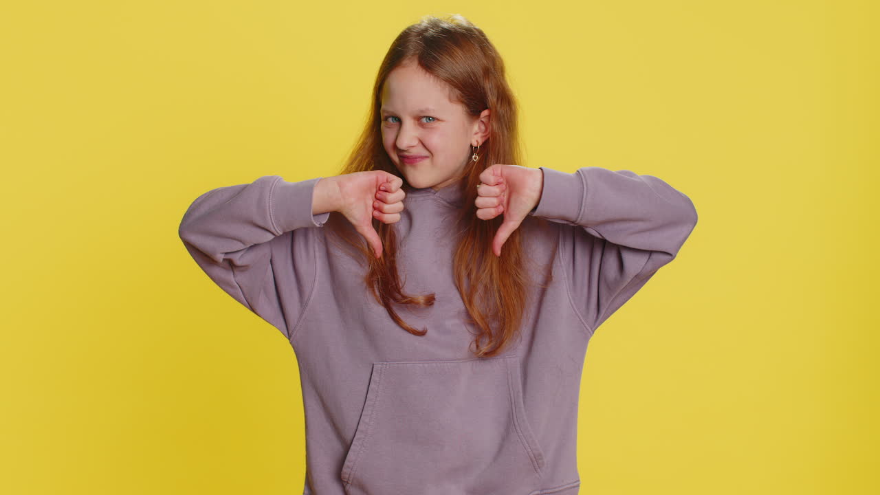 Upset preteen child girl showing thumbs down dislike bad work disapproval dissatisfied feedback