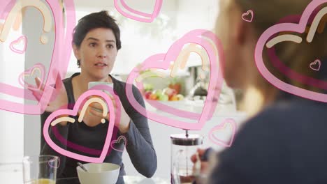 animation of hearts over caucasian female couple eating breakfast