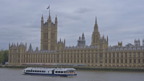 boat sailing along river thames with palace of westminster in background, london