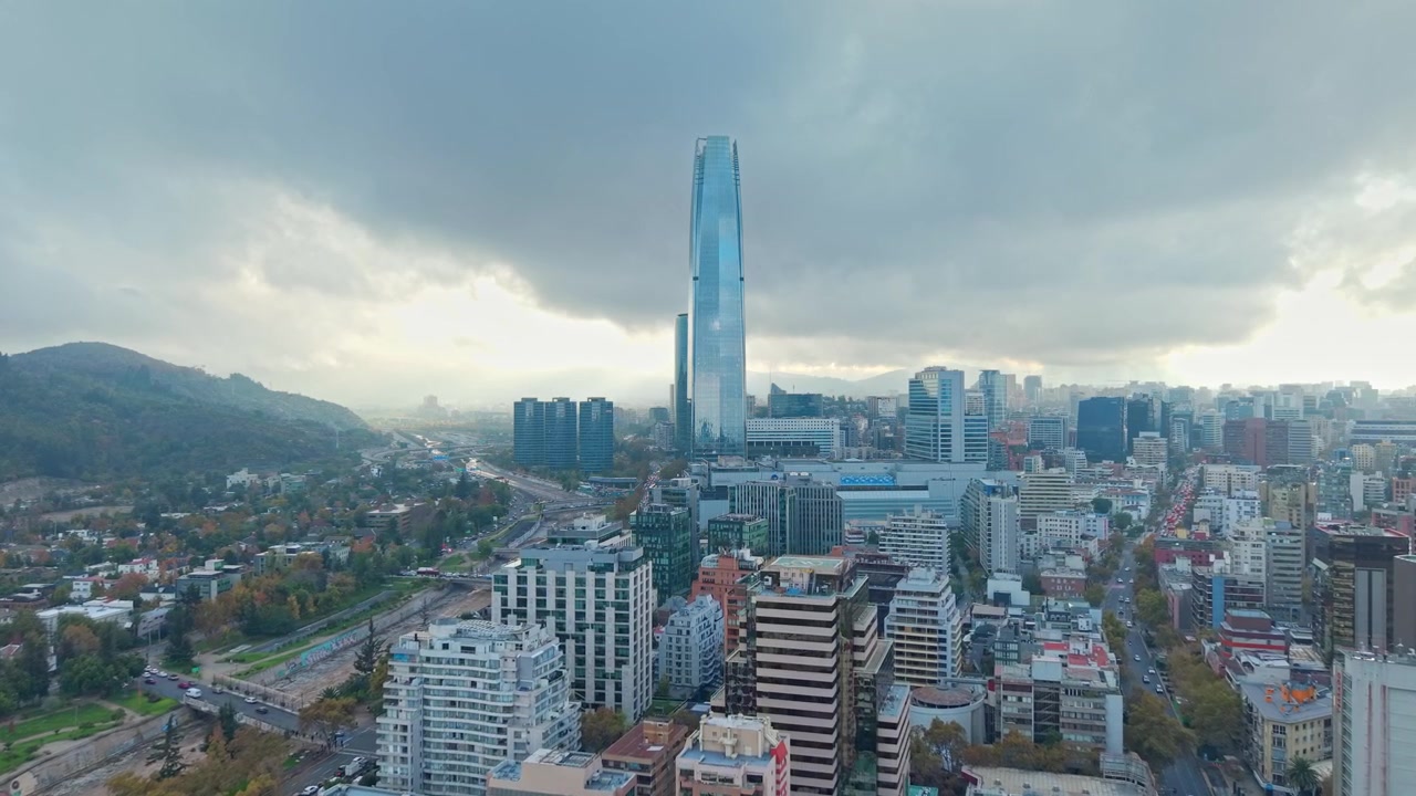Vista aerea con carrellata in avanti del quartiere di Providencia con l'alta Torre Costanera, un edificio moderno a Santiago, Cile, in una mattina con una grande nuvola grigia.