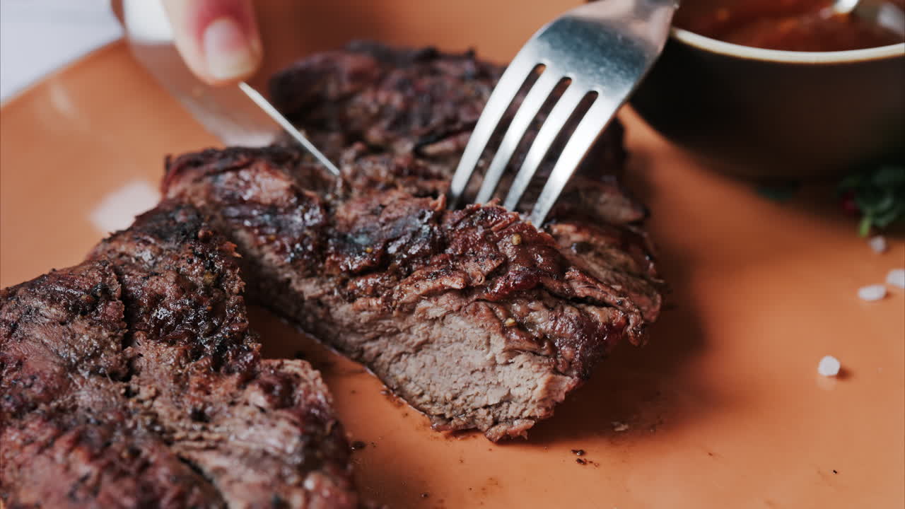 Close up of a woman's hands cutting a Sirloin Steak with Barbecue Sauce and micro-plants on the side