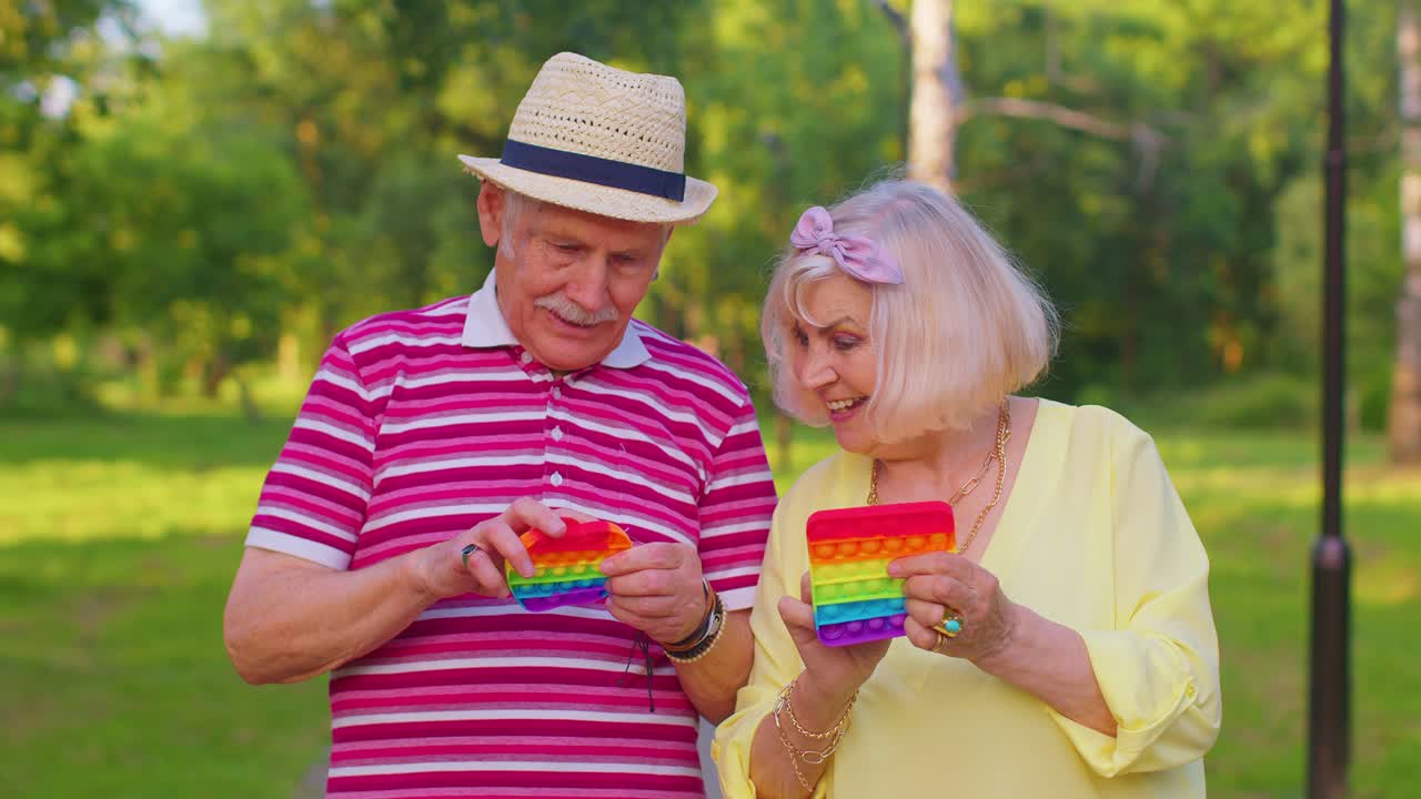 Abuelos sonrientes jugando con un juguete antiestrés popular 'push pop it' de pantalla táctil.