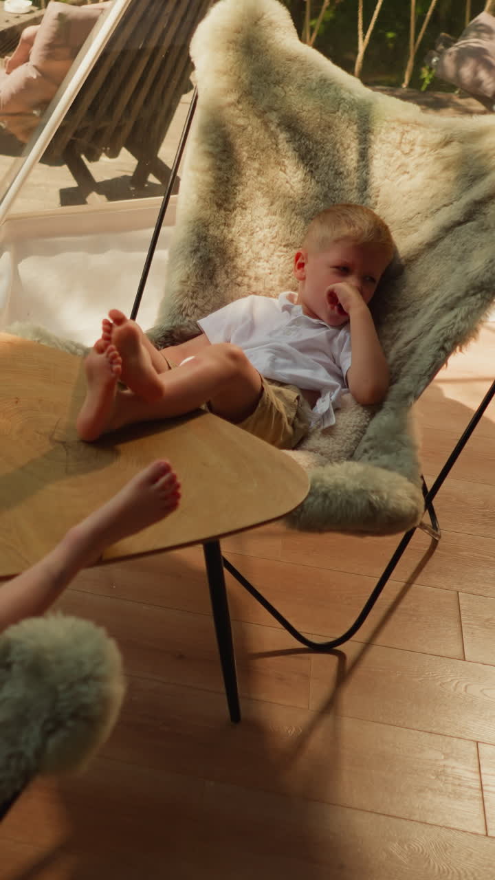 los niños pequeños descansan juntos en la terraza de glamping. el niño pequeño cansado con la hermana se sientan en sillas cómodas bajo una cúpula clara. los niños en vacaciones de verano