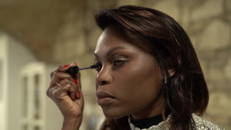 slowmotion shot as a model, black woman applying makeup, fixing her eyelashes