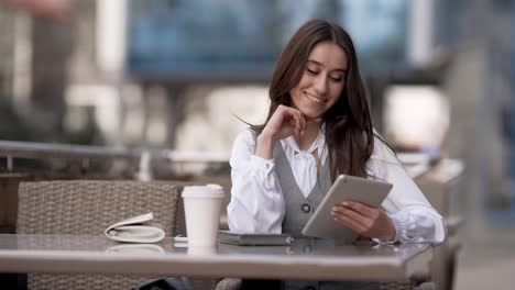 young business woman sitting on summer terrace of cafe with tablet smiling