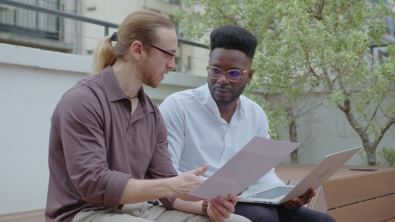 compañeros de trabajo trabajando con portátiles y documentos en la terraza al aire libre