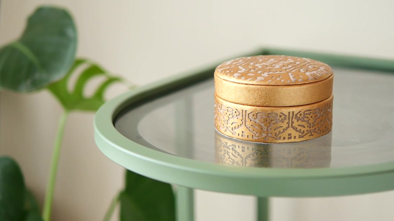 Main ramassant une boîte dorée ornée sur une table d'appoint verte