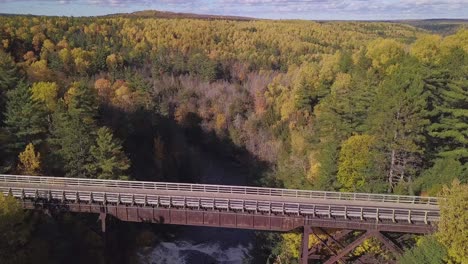 Forward-aerial-of-bridge-over-Agate-Falls,-MI,-and-colorful-forest