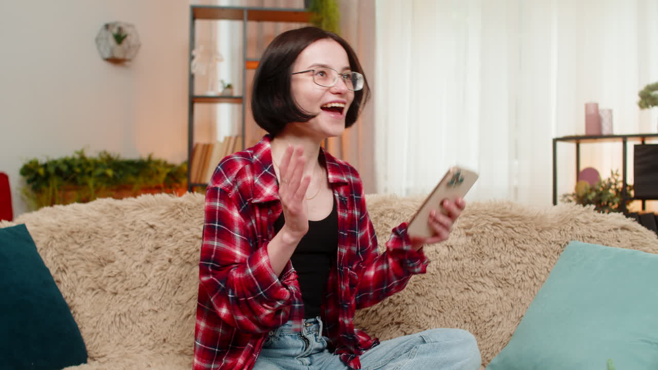 Young smiling woman using smartphone at home winning online lottery game celebrating jackpot victory