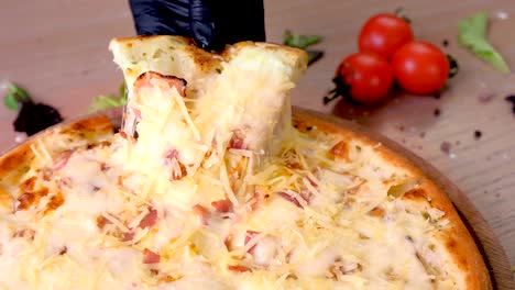 Cook takes a slice of bacon pizza with melted cheese, hands in rubber gloves.