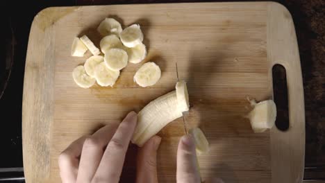 Ansicht-Von-Oben---Frauenhand-Schneidet-Eine-Reife-Banane-Auf-Holzschneidebrett