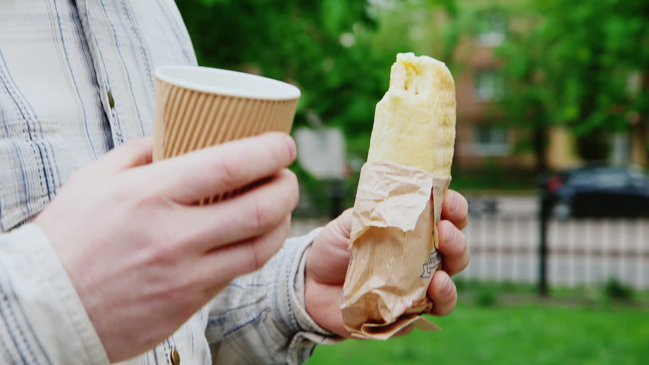 un hombre camina por la calle con un café y un sándwich en el marco solo se ven las manos
