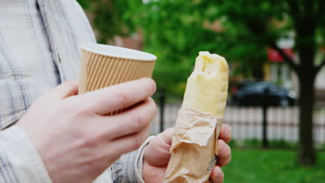 a man walks down the street with a coffee and a sandwich in the frame only hands visible