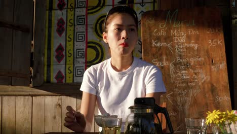 Front-view-of-young-Asian-woman-eating-ice-cream-alone-sitting-at-table,-Vietnam