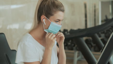 una joven deportista se pone una máscara facial y usa una máquina de ejercicios en el gimnasio