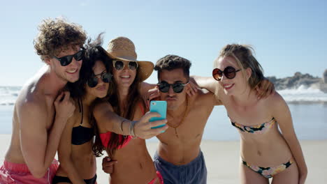 mixed race group of friends taking selfies on the beach using phone camera