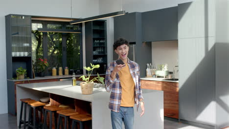 talking on smartphone, teenage boy smiling and walking in modern kitchen