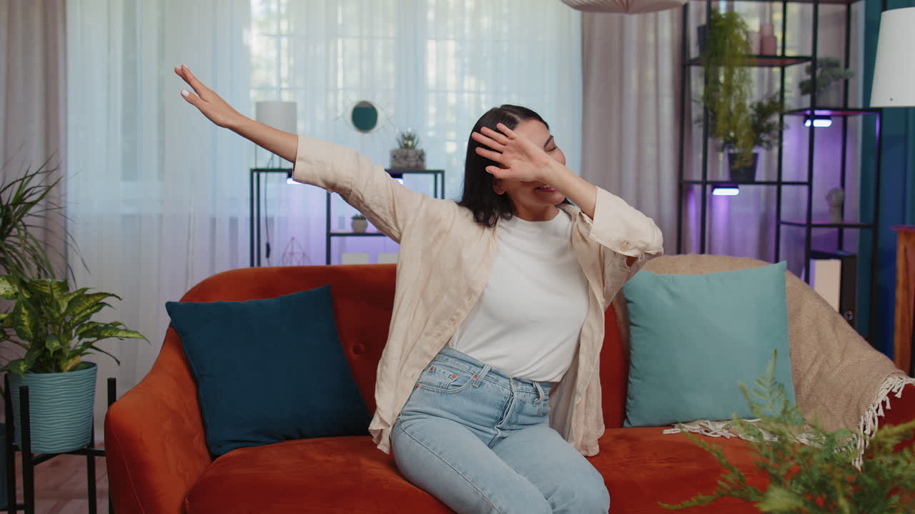 Trendy cheerful positive woman dancing and moving to rhythm making dub dance gesture at modern home
