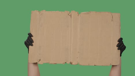 un espacio de copia de banner de protesta. una mujer sostiene un cartón en blanco en su mano. plataforma publicitaria. mano en un guante médico negro aislado en un fondo verde, chromakey. primer plano. cámara lenta