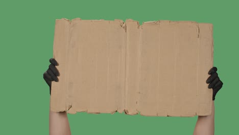 protest banner copy space. a woman holds a blank cardboard in her hand. advertising platform. hand in a black medical glove isolated on a green background, chromakey. close up. slow motion