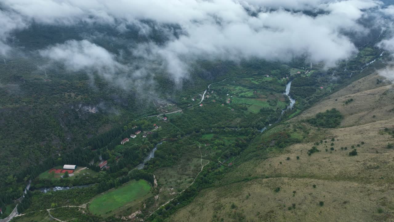 HIgh angle view of a town situated in middle of mountains wih clouds on top in Cetinje, Montenegro. Drone shot.