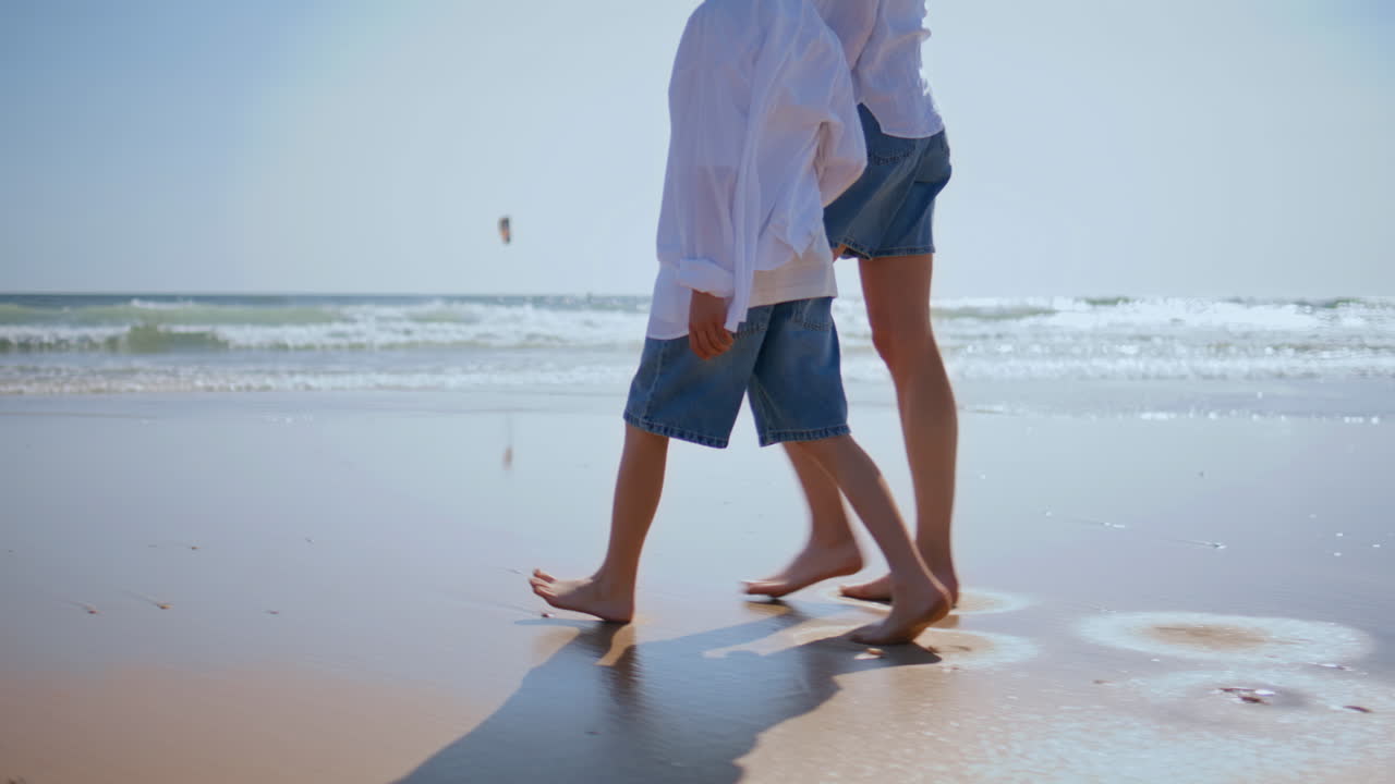 Mother boy walking barefoot on wet sand by sea closeup. Woman son strolling