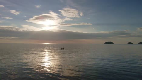 Aerial-drone-left-orbit-shot-of-tropical-Islands-silhouetted-at-sunset-with-small-fishing-boat-with-light-reflection-on-ocean